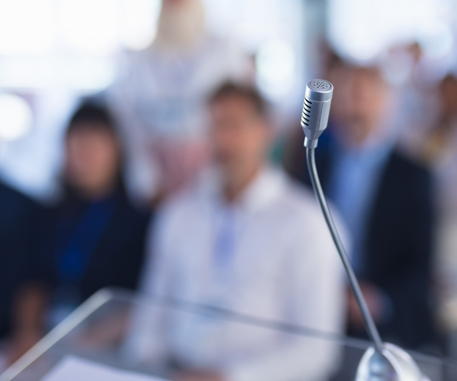 Mikrofon im Vordergrund, Zuhörende im Hintergrund eines Konferenzraums