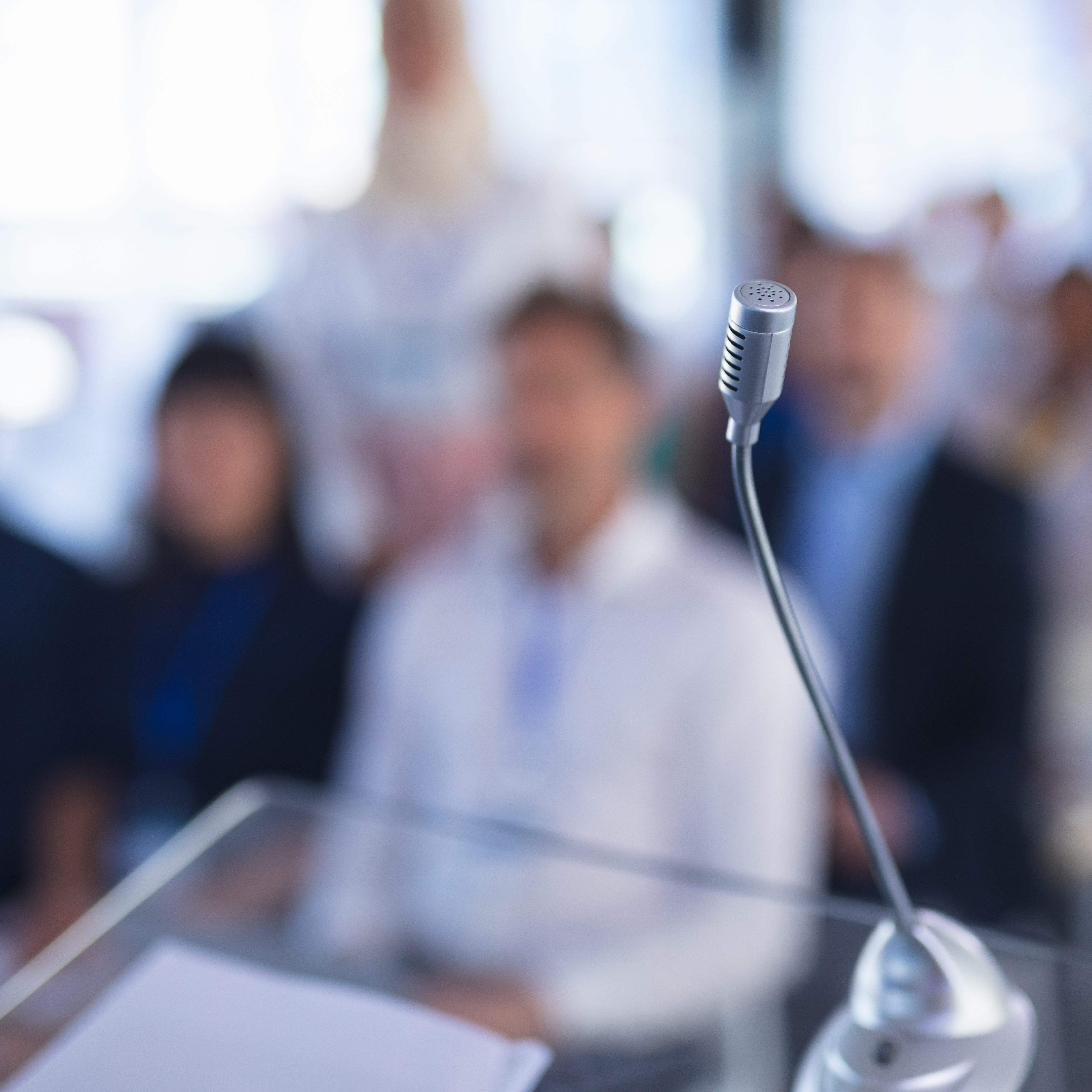 Mikrofon im Vordergrund, Zuhörende im Hintergrund eines Konferenzraums