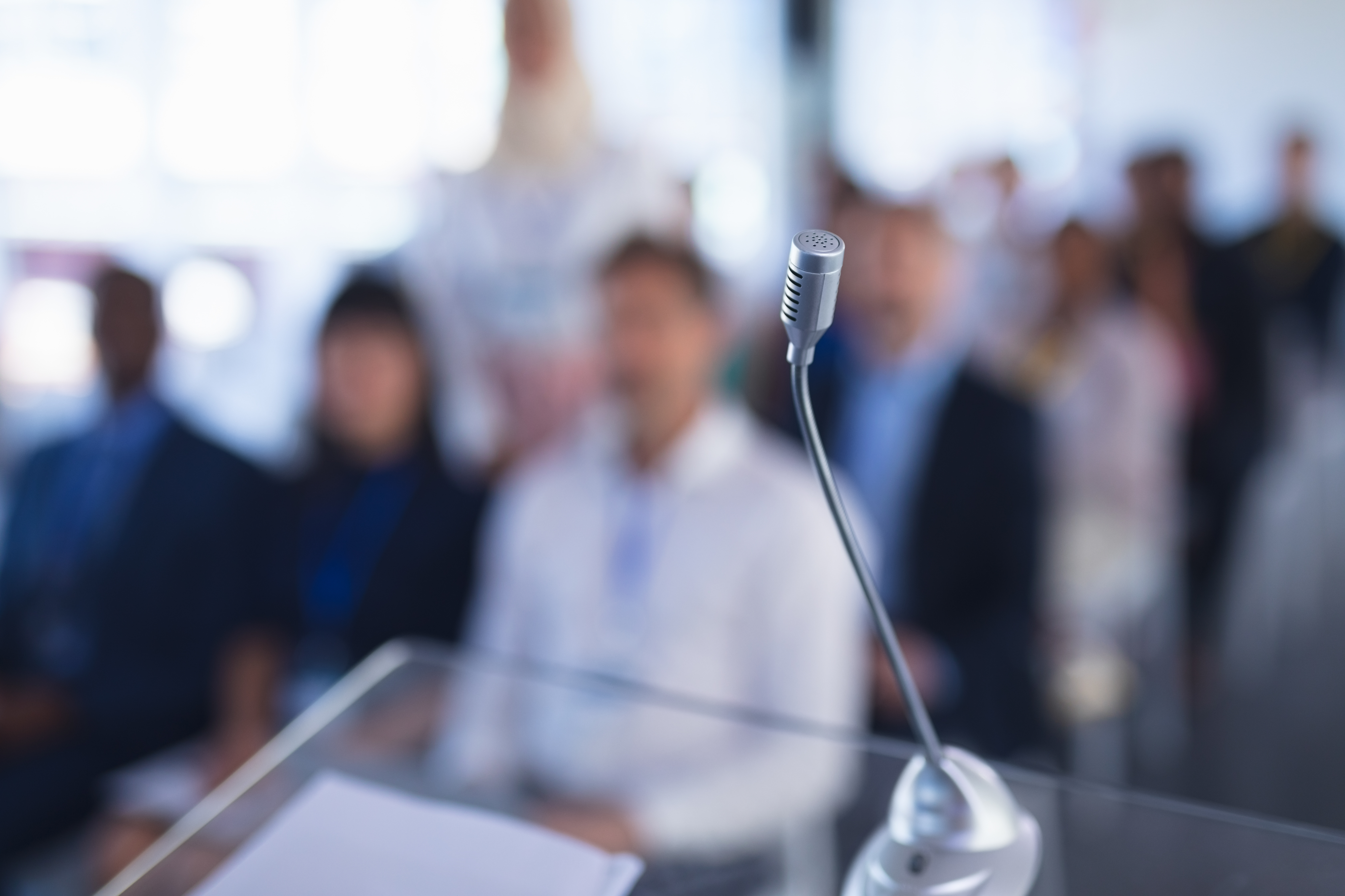 Mikrofon im Vordergrund, Zuhörende im Hintergrund eines Konferenzraums